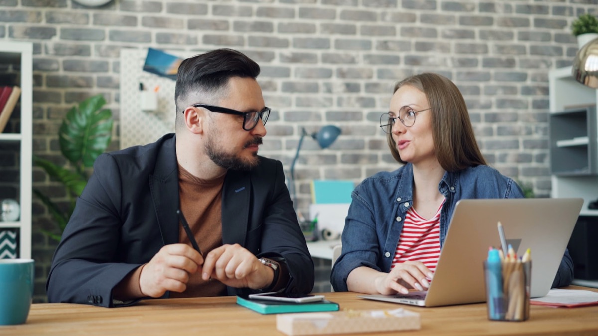 Two people talking through the work at a table, laptop open between them